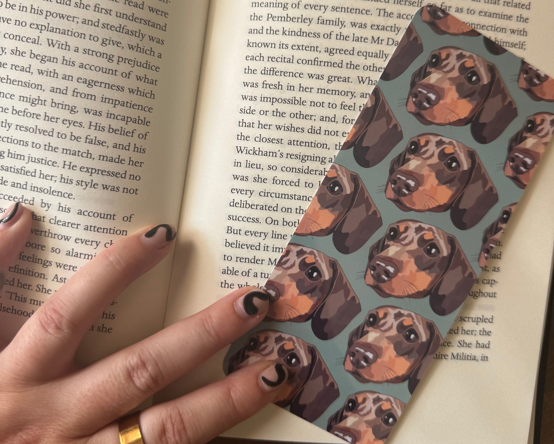 Open book with a hand holding a bookmark featuring dachshund dog pattern.