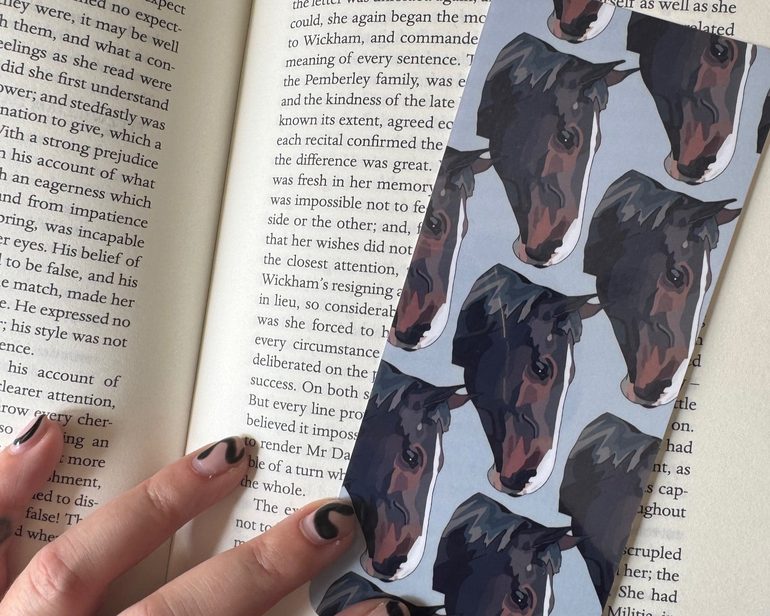 Hand holding a horse portrait bookmark over an open book