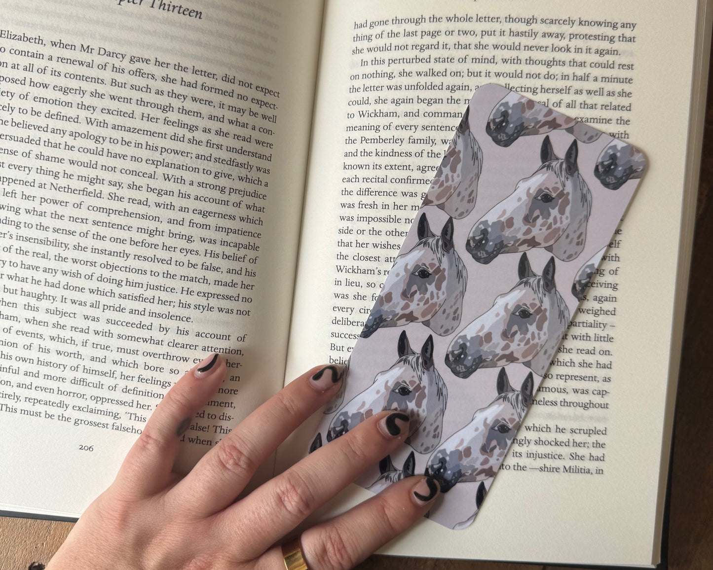 Hand holding a patterned bookmark over an open book on a wooden surface