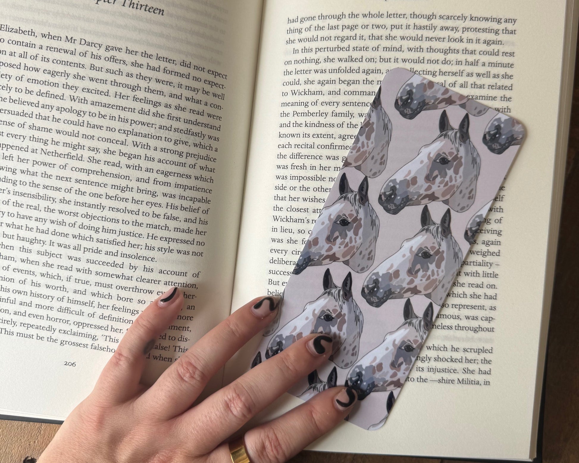Hand holding a patterned bookmark over an open book on a wooden surface