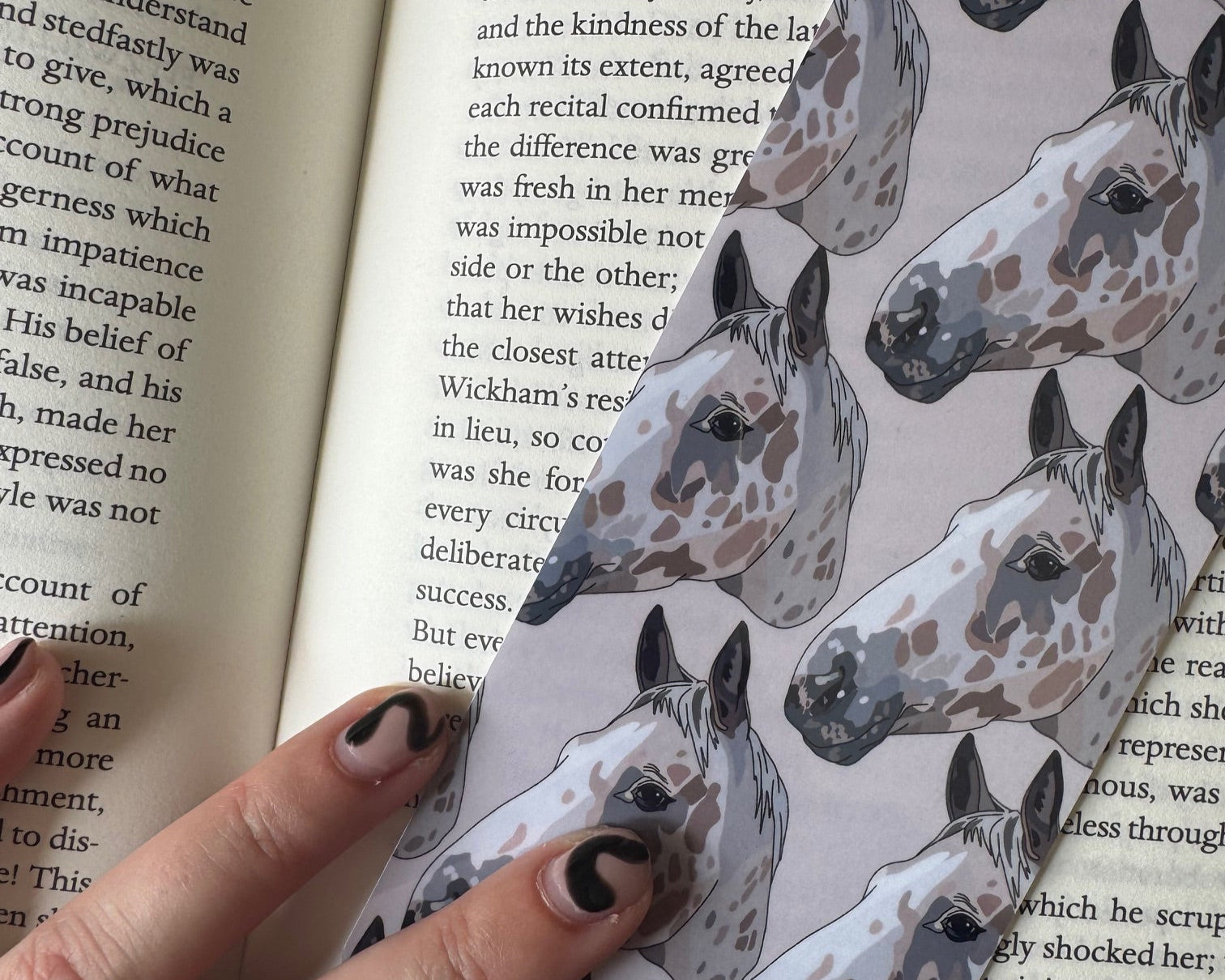 Hand holding a paper with horse illustrations over an open book